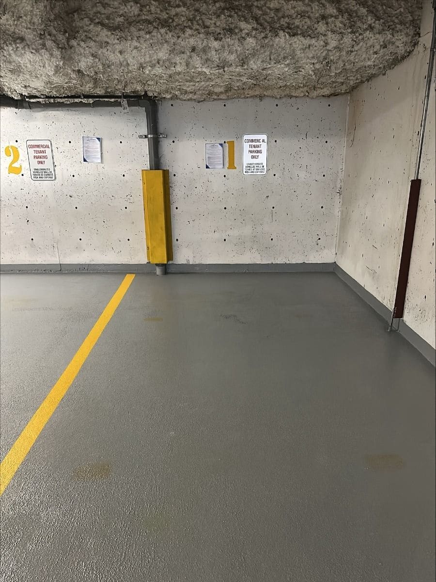A parkade stall finished in a textured grey traffic coating, with a yellow stall line and the coating carried up the base of the wall
